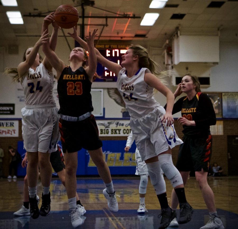 two girls basketball player in white on either side of a player in black with everyones hands on the ball