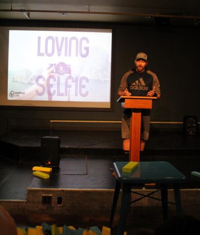 A man at a podium in front of a presentation reading "love your selfie"