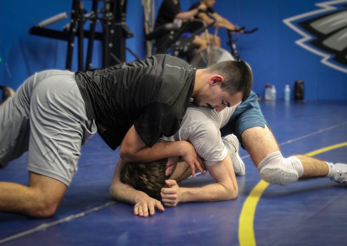 Photo taken of wrestlers Chase Campbell and Darren Mitchell fighting to gain dominant position during a long, hard practice while basketball fans filled the bleachers for a home game. Photo taken by assistant coach Justa Curtice in December 2025. 